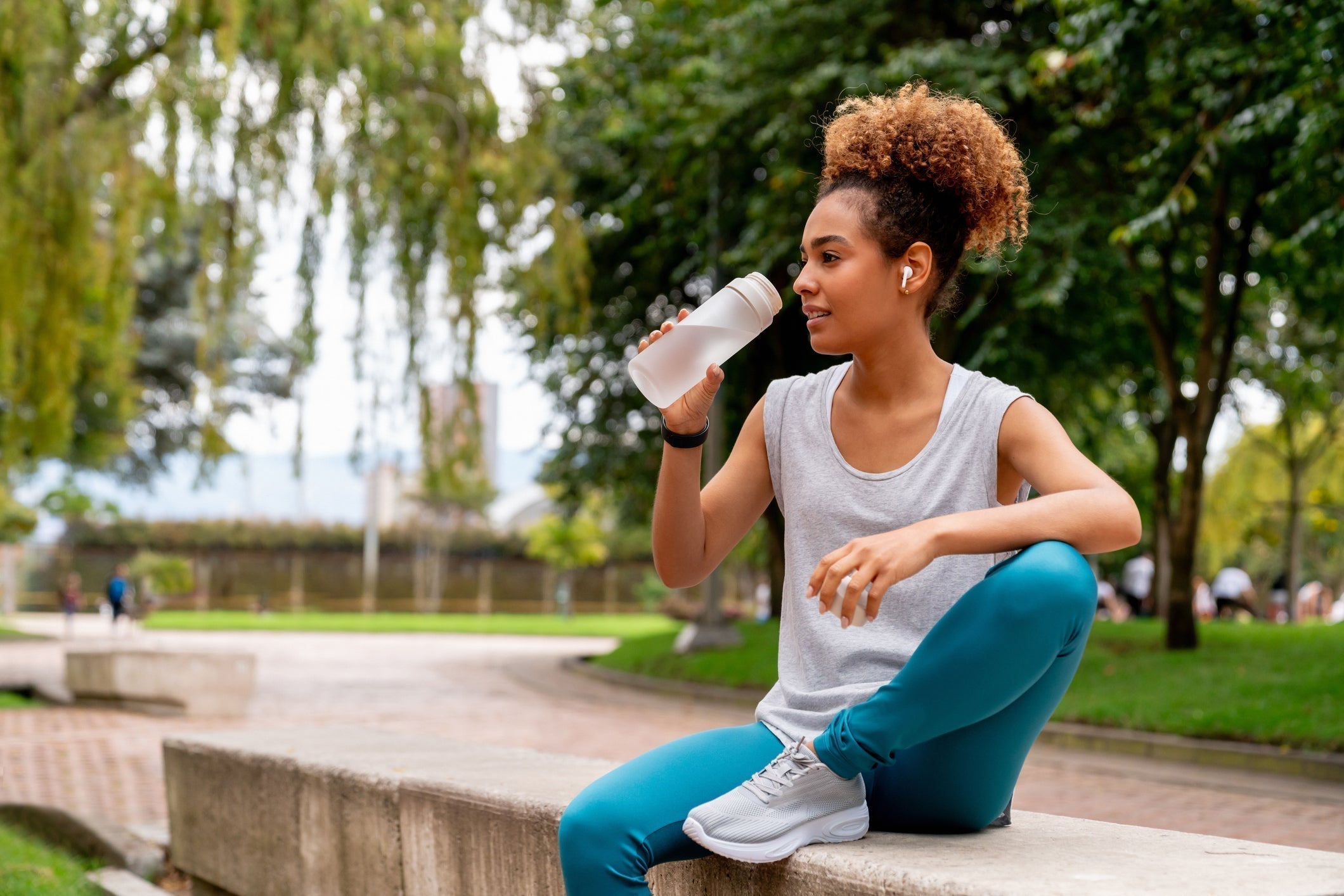 Woman refilling a glass water bottle at her kitchen counter next to a Biocare protein shake